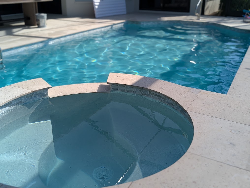 Pool and attached round spa with mosaic tile and travertine deck
