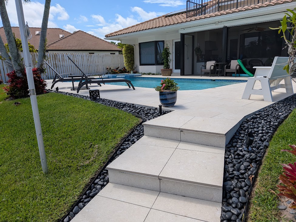 Backyard pool with travertine paver deck, stone borders, and lush lawn by MBG&A