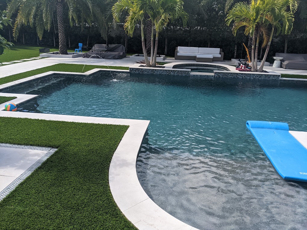 Backyard remodel with dark-finish pool, spa, turf inlays, and travertine deck by MBG&A