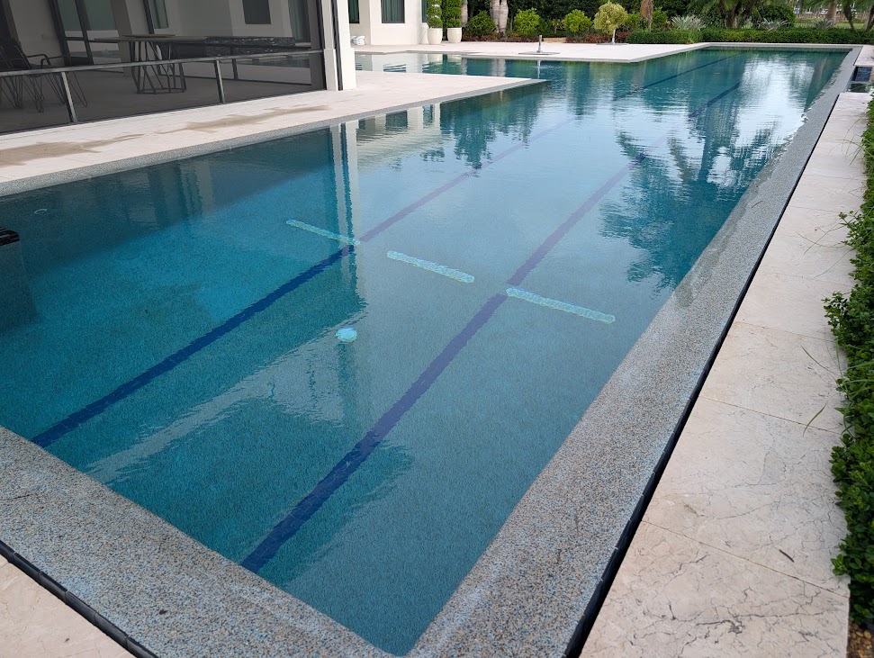 Lap pool with dark racing lanes and travertine coping by MBG&A